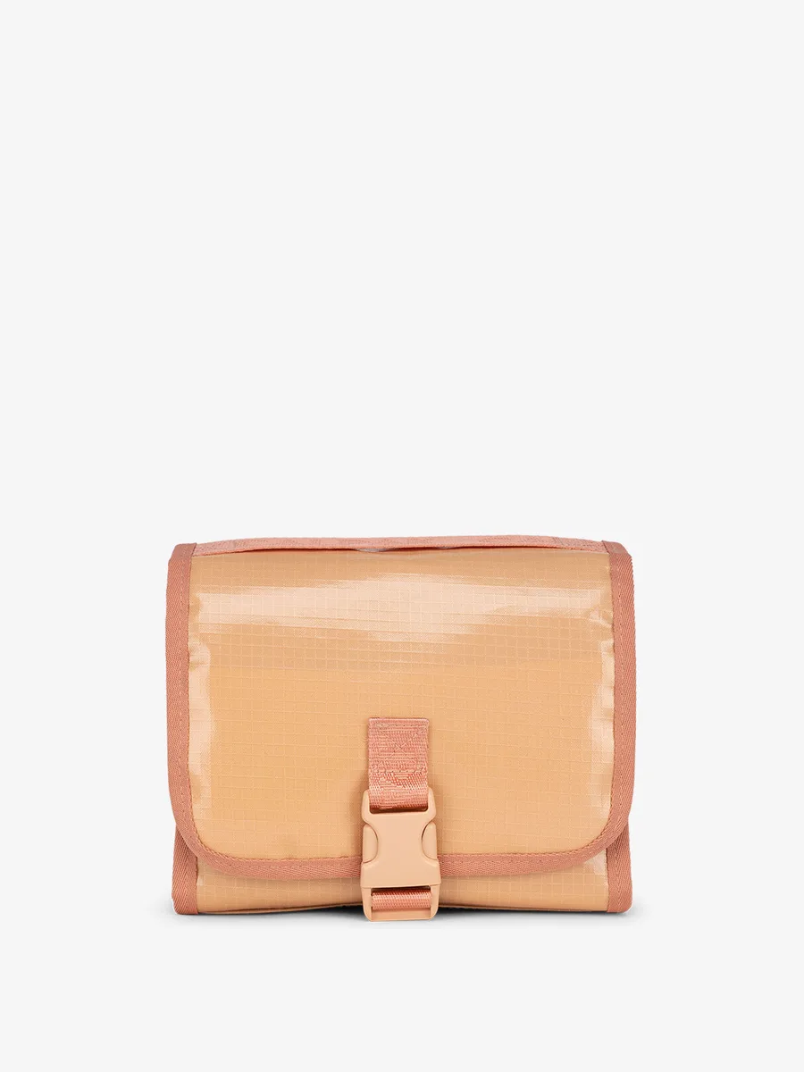 The CALPAK Terra Hanging Toiletry Bag in a tan canyon colorway, folded closed with its buckle clip fastened