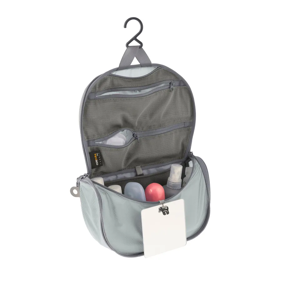 The Sea to Summit Ultra-Sil Hanging Toiletry Bag in grey, unzipped and hanging from its hook, showing mesh pockets, travel bottles, and the detachable mirror